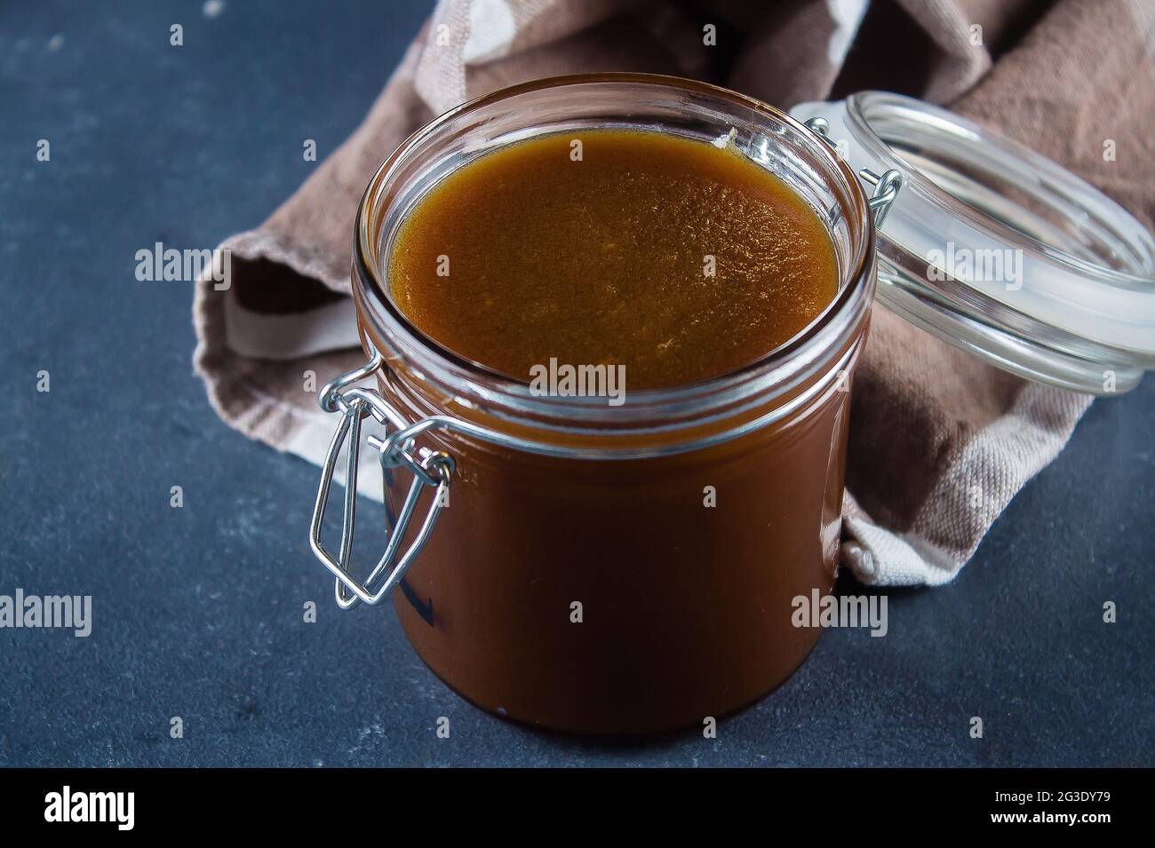 Homemade salted caramel sauce in jar on blue concrete table background. Copy space Stock Photo