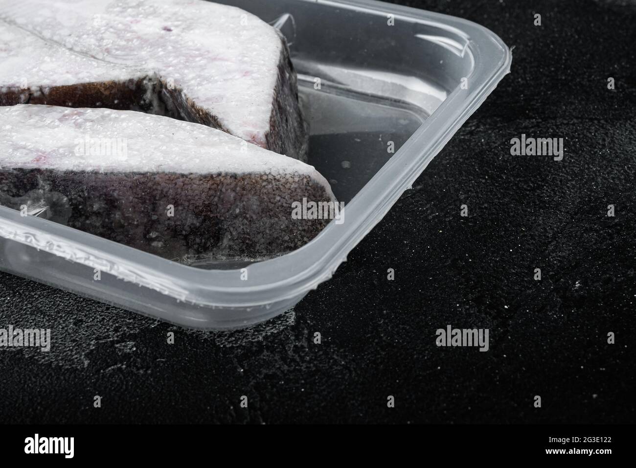 Frozen Greenland halibut steaks vacuum pack set, on black dark stone
