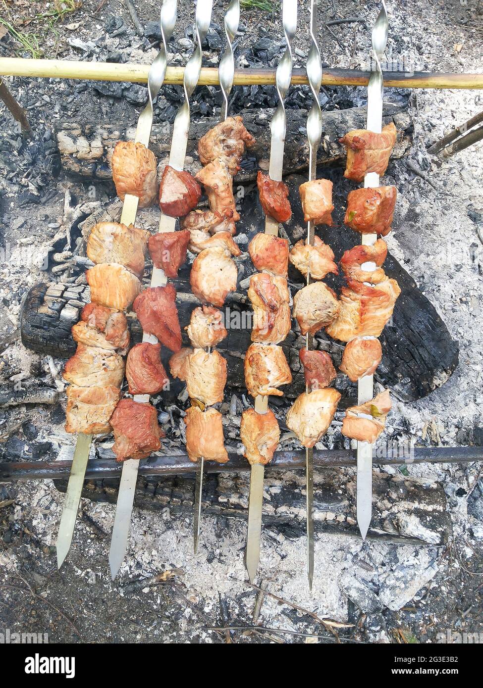 Six skewers with meat are fried on a fire in the forest Stock Photo