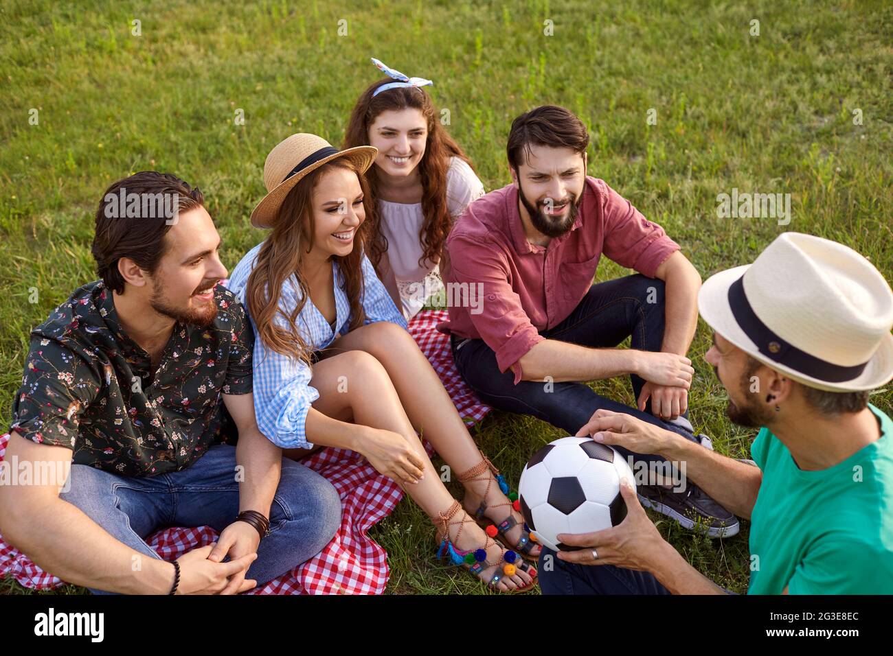 A group of young friends are having fun talking while sitting on the grass while relaxing in a summer park. Stock Photo