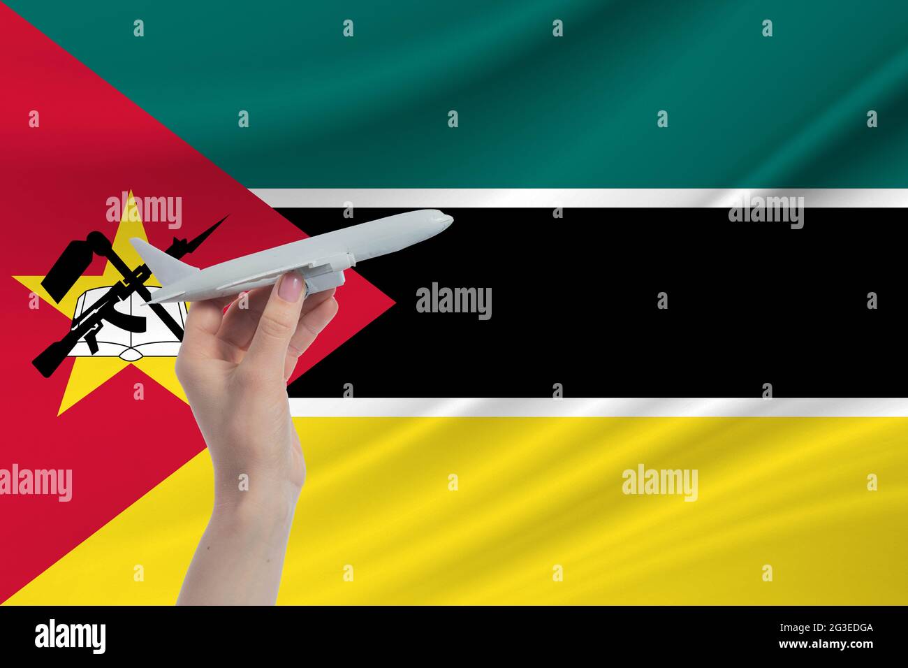 Airplane in hand with national flag of Mozambique. Travel to Mozambique. Stock Photo