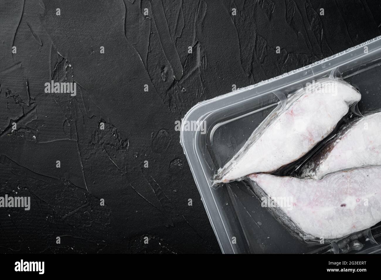 Frozen Greenland halibut steaks vacuum pack set, on black dark stone ...