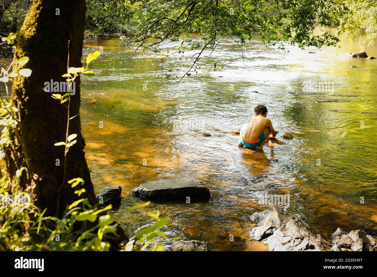 Young boy sitting and playing in the river back view Stock Photo - Alamy