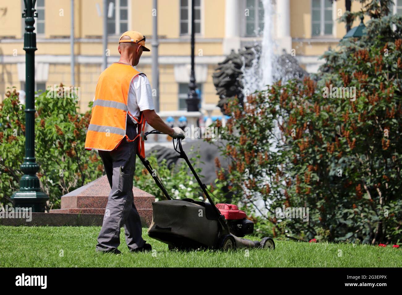 Gardener mowing the grass with lawn mower at summer. City park improvement in sunny day Stock Photo