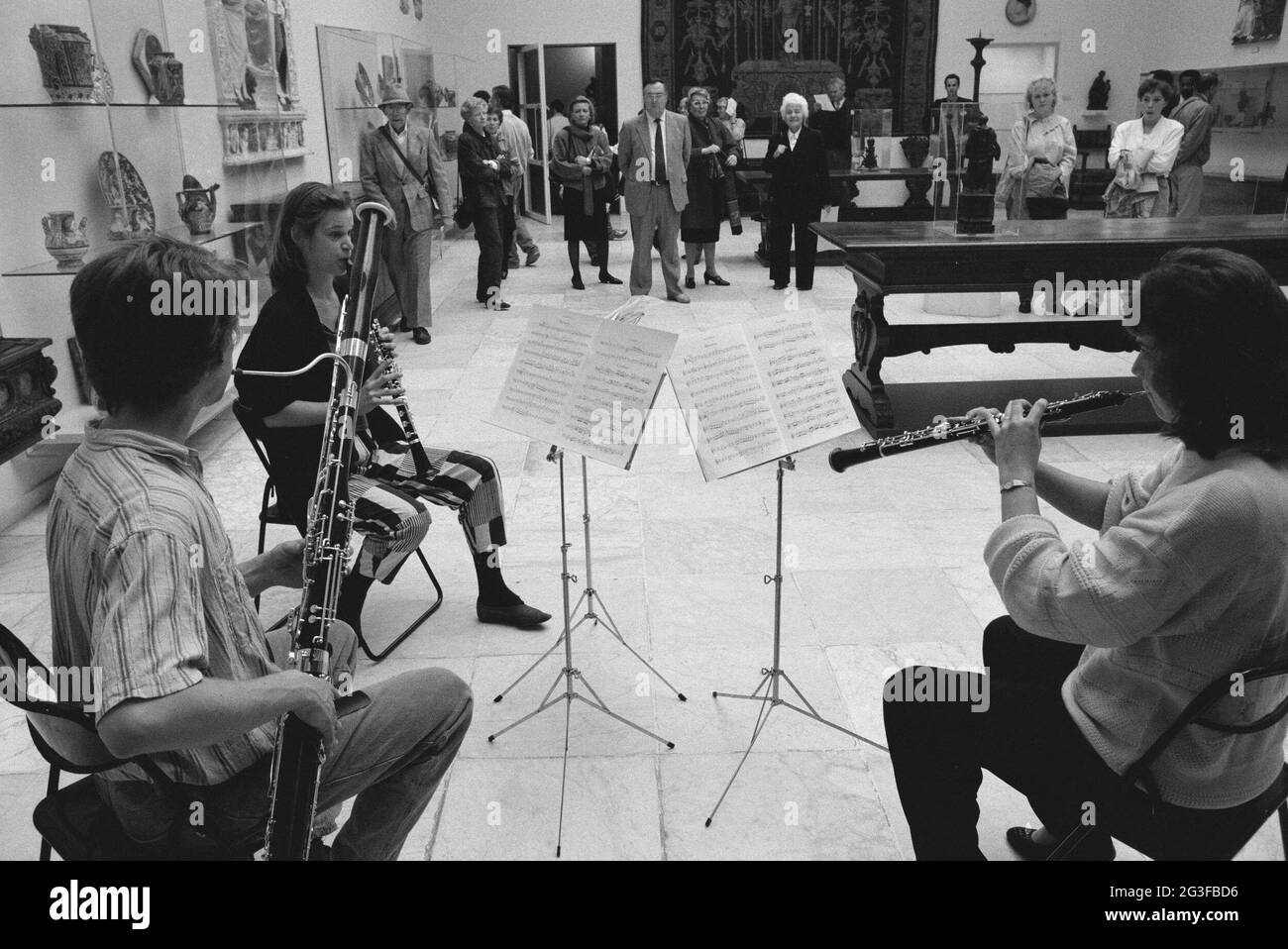 Sitting man and two women playing wind instruments while public watches ...