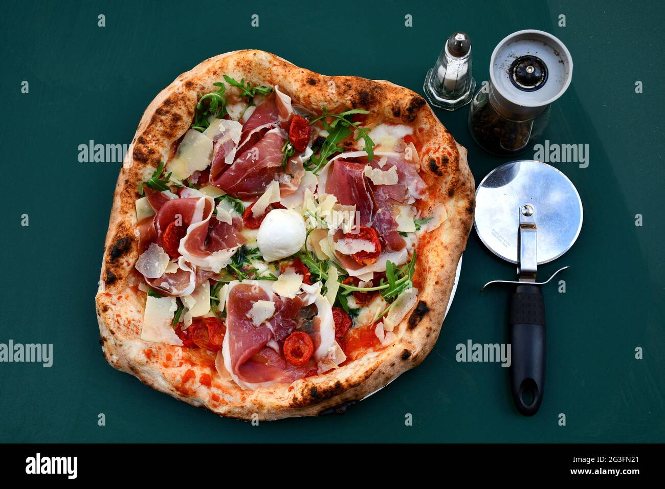 Closeup shot of freshly baked pizza, cutter, and condiments isolated on a dark-green background Stock Photo