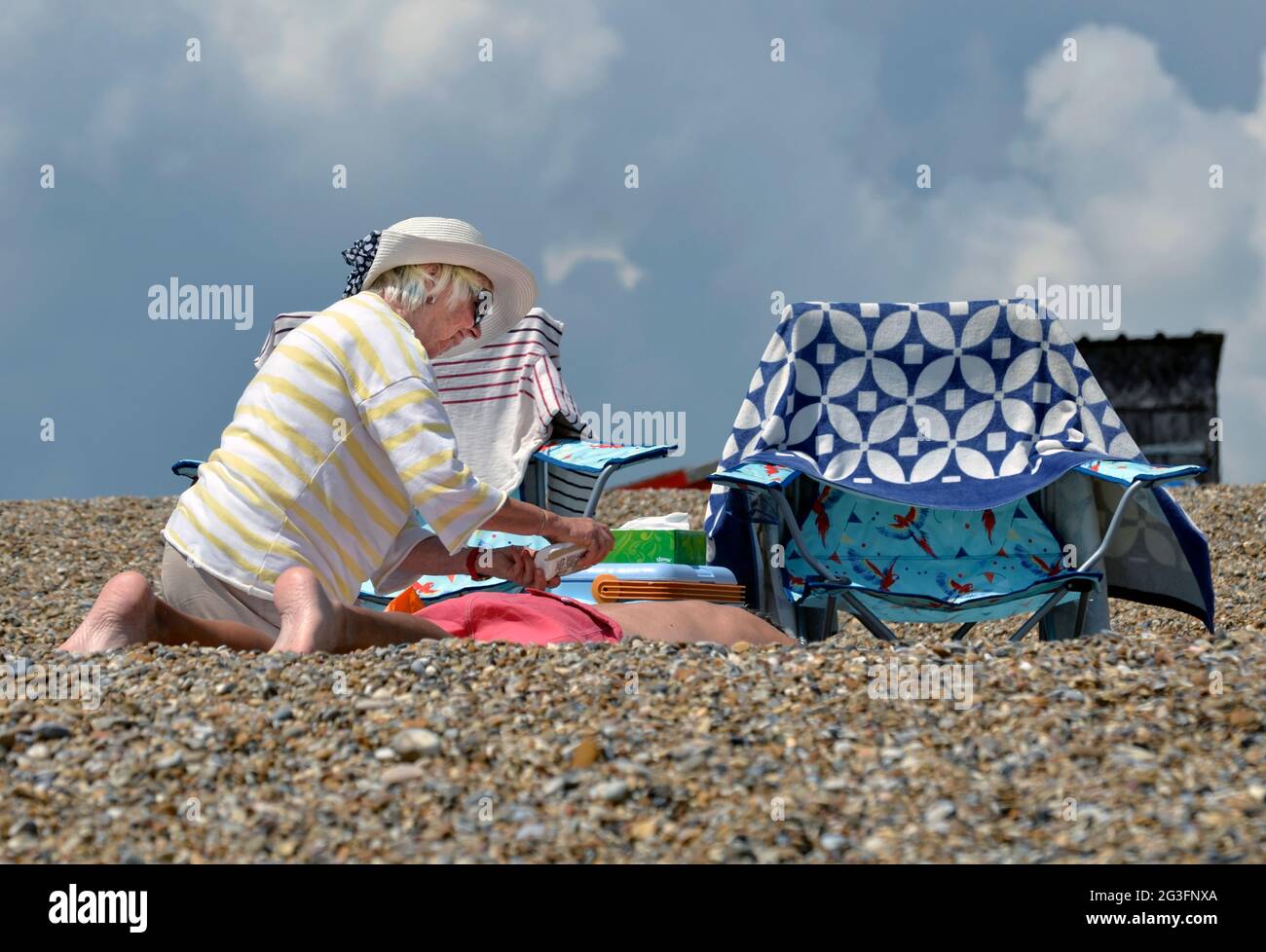 older woman applying sun tan oil to husband on dunwich beach suffolk england Stock Photo