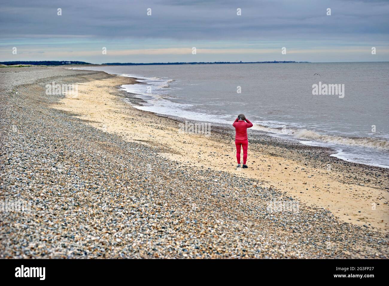 woman in red on sizewell beach looking out to sea towards southwold with binoculars suffolk england Stock Photo