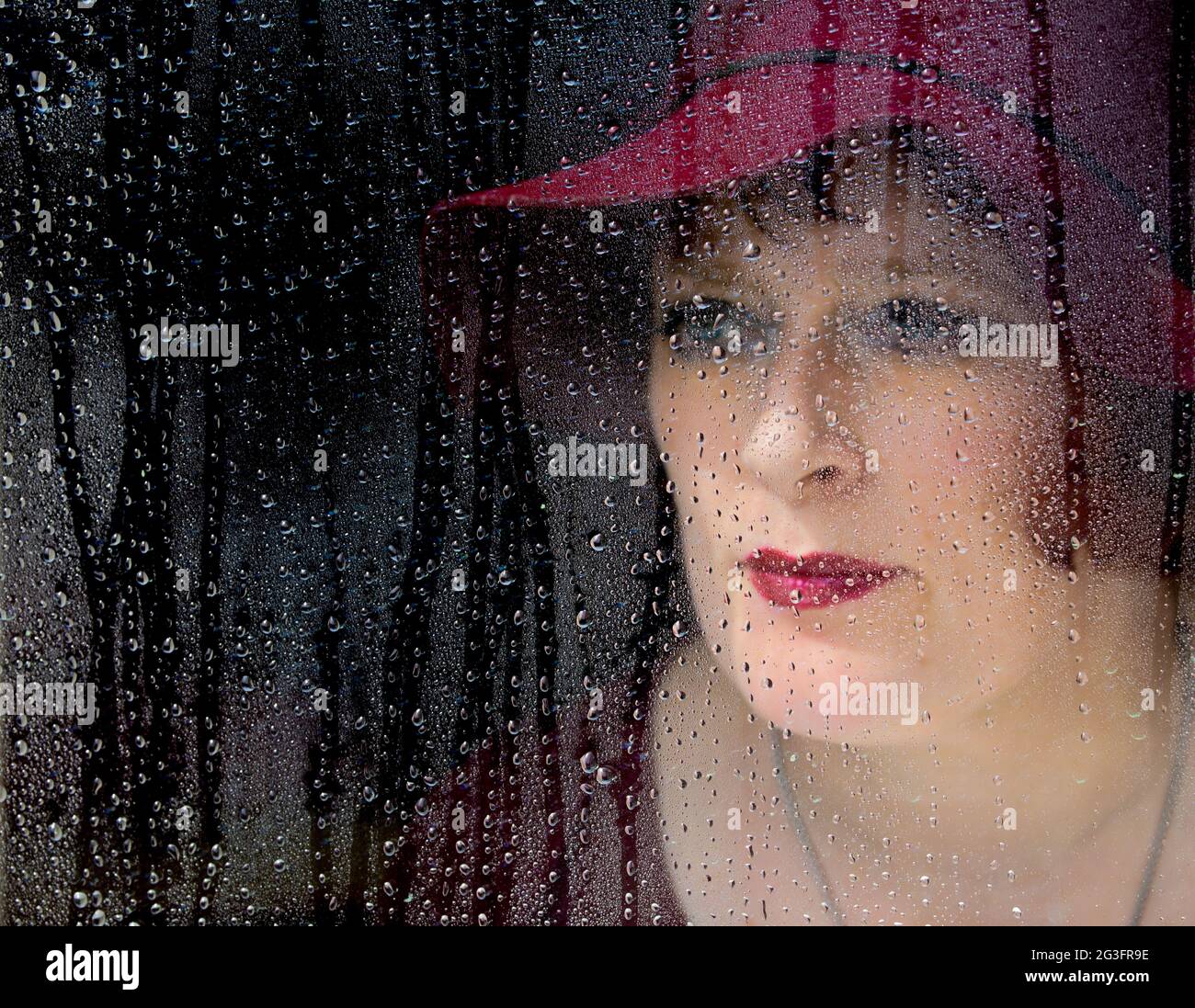 Woman looking through window covered with raindrops. Stock Photo