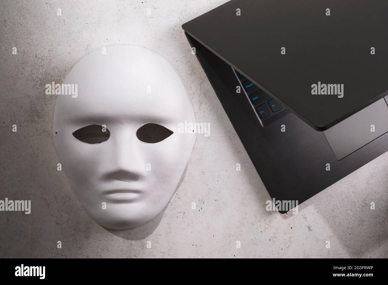 White mask and laptop on the table, top view, anonymity