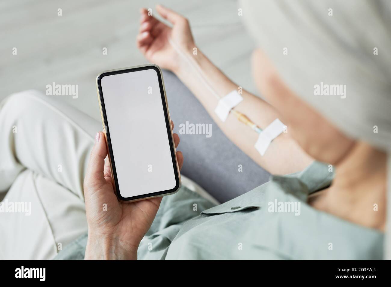 Minimal close up of unrecognizable woman getting IV drip and using smartphone with blank screen, copy space Stock Photo