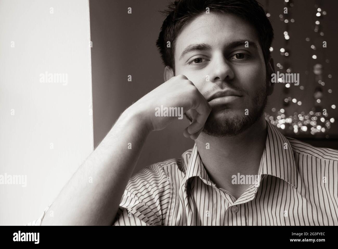 Portrait of attractive man with beard sitting next to window with lights in the background Stock Photo