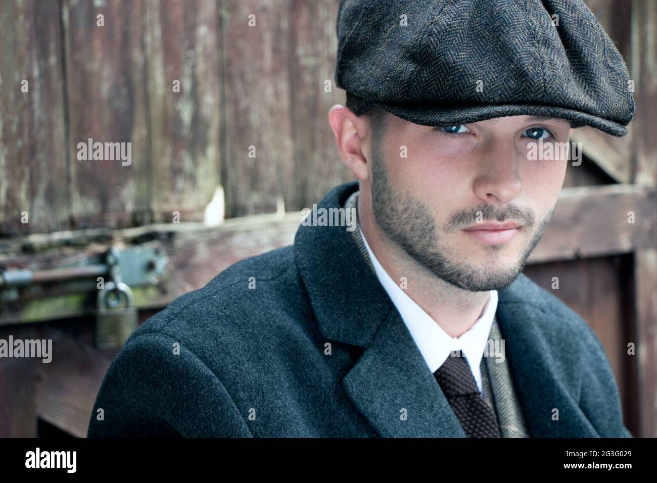 Portrait of attractive English gangster in costume with waistcoat, tie and cap and leaning on gate Stock Photo