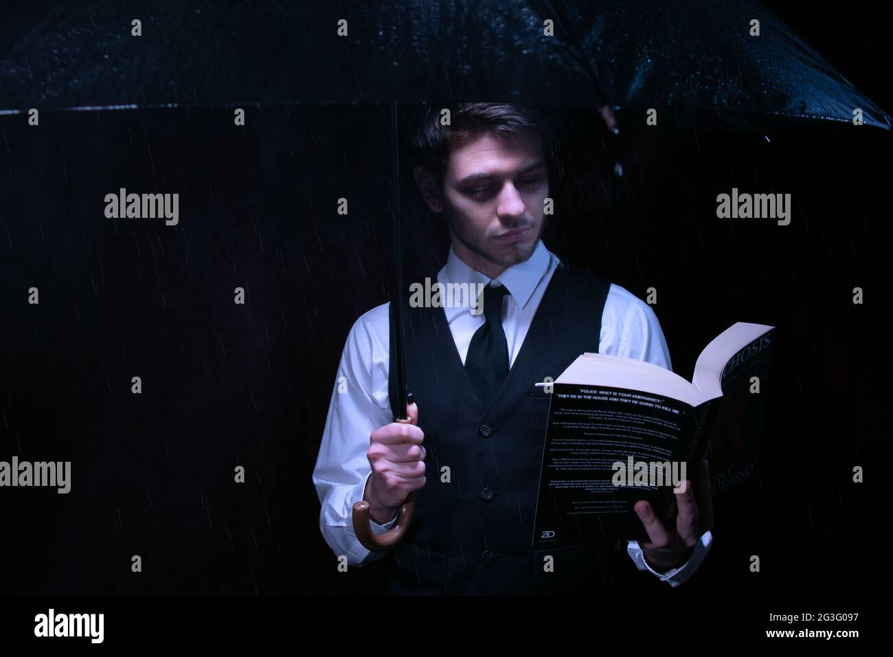 Man dressed in suit and tie holding unbrella and reading book Stock Photo
