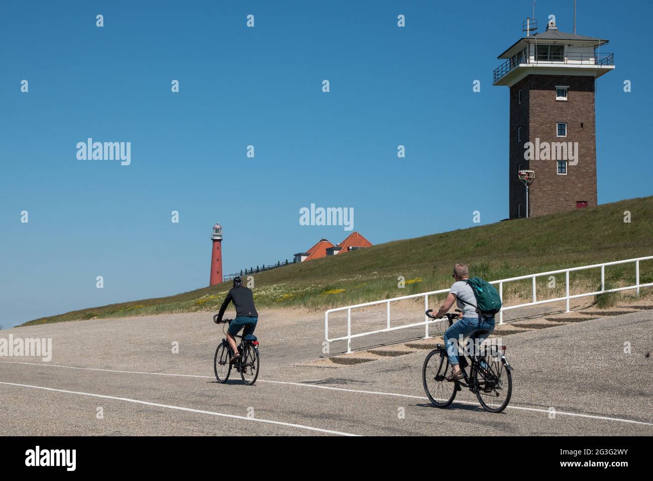 Cyclists on the dike near Huisduinen, Den Helder, with Lange Jaap lighthouse and the coast guard tower in the background. High quality photo Stock Photo