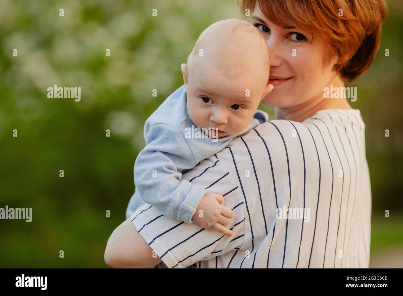 Side view of smiling loving mother with cute infant in green summer park Stock Photo