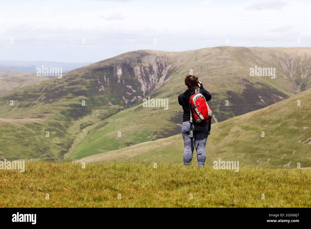Woman photographs from Arant Haw in the Yorkshire Dales National Park. She looks towards nearby hills. Stock Photo