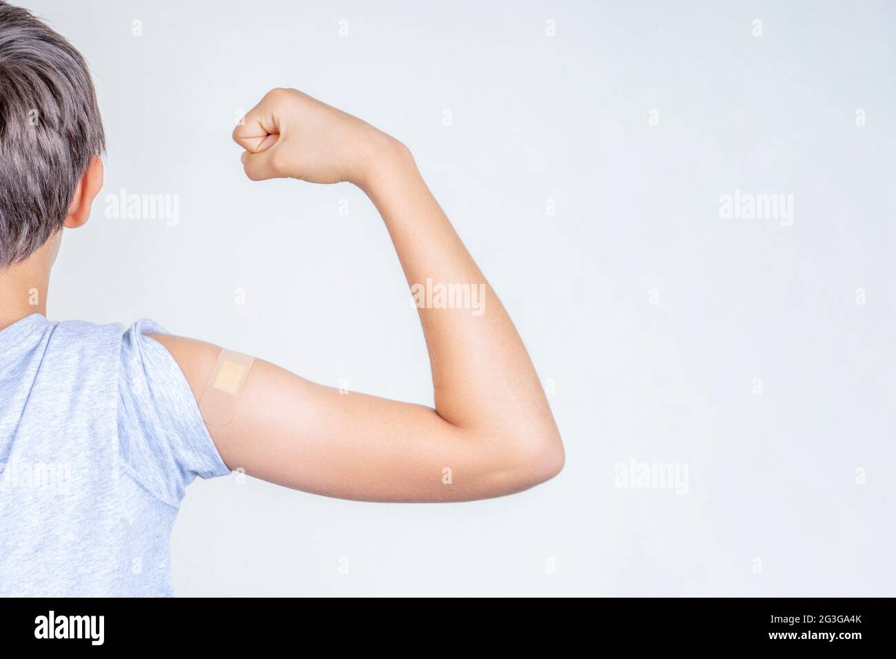 Teenage boy with bandage plaster on his arm makes fist and flexes her bicep after vaccination. Injection covid vaccine, healthcare for children Stock Photo