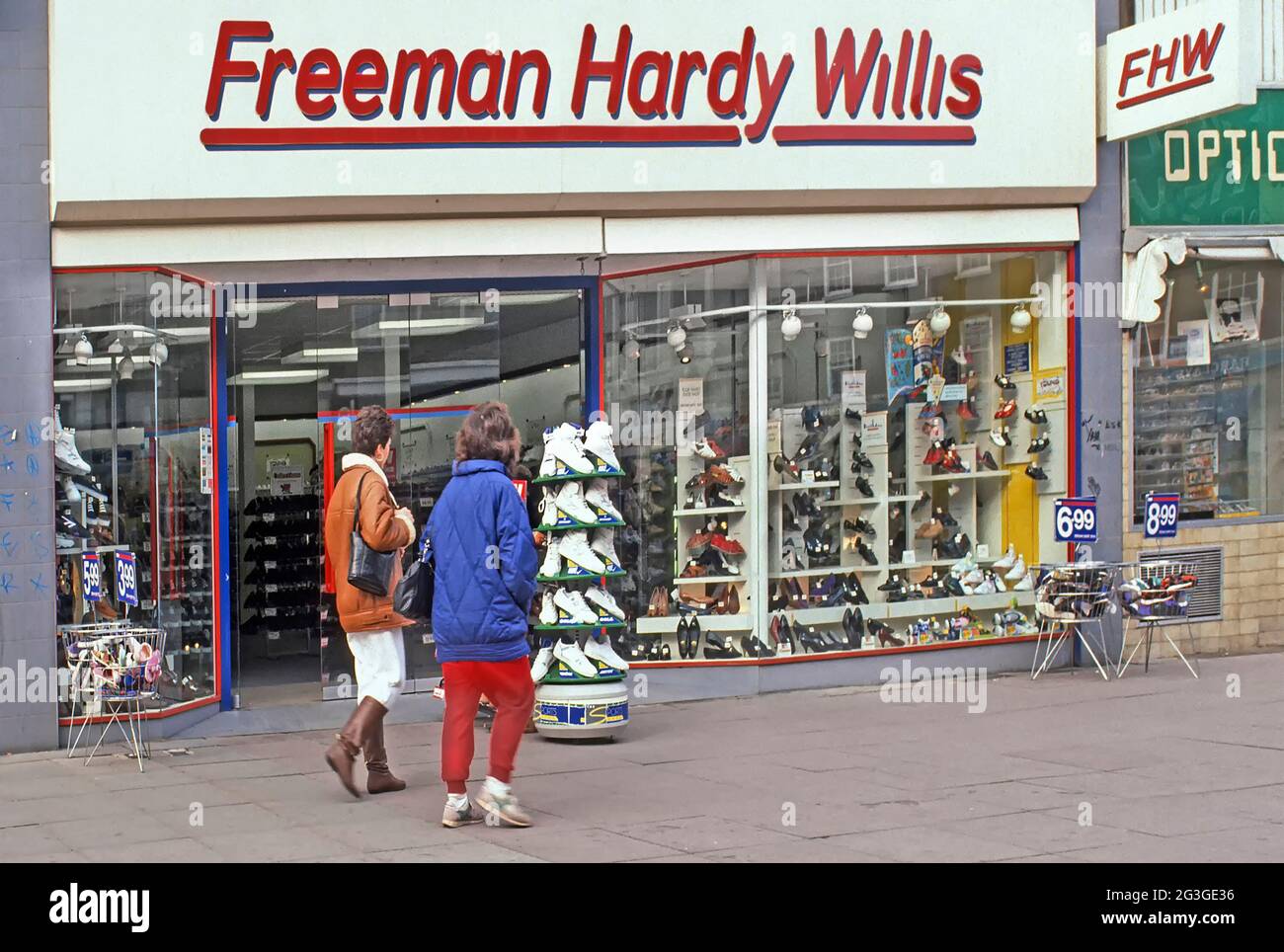 Freeman Hardy Willis FHW shoe store brand shop front window 1991 archive historical street scene view couple of women shoppers walking along shopping street pavement outside 1990s display of a retail footwear business in London Borough of Barking archival image of the way we were in 90s East End England UK Stock Photo