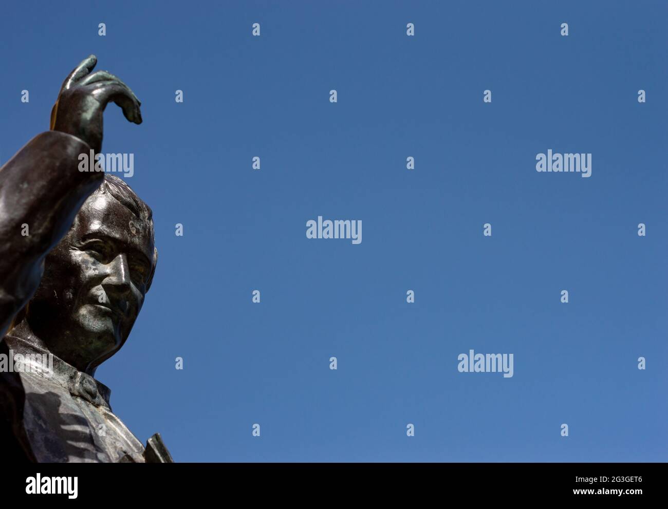 Old Bronze statue of a Saint with an hand up to the blue sky Stock Photo