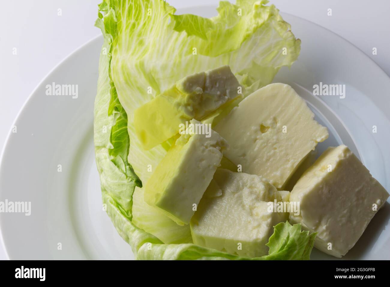 Feta cheese cubes on lettuce leaf close up - white background with soft curd cheese Stock Photo