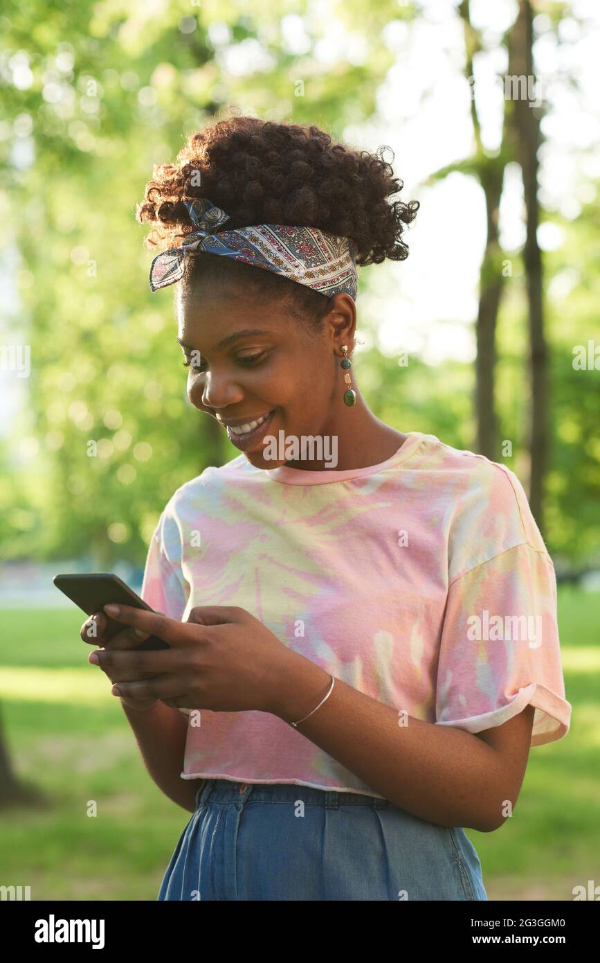 African happy woman talking online using her mobile phone while standing in the park Stock Photo