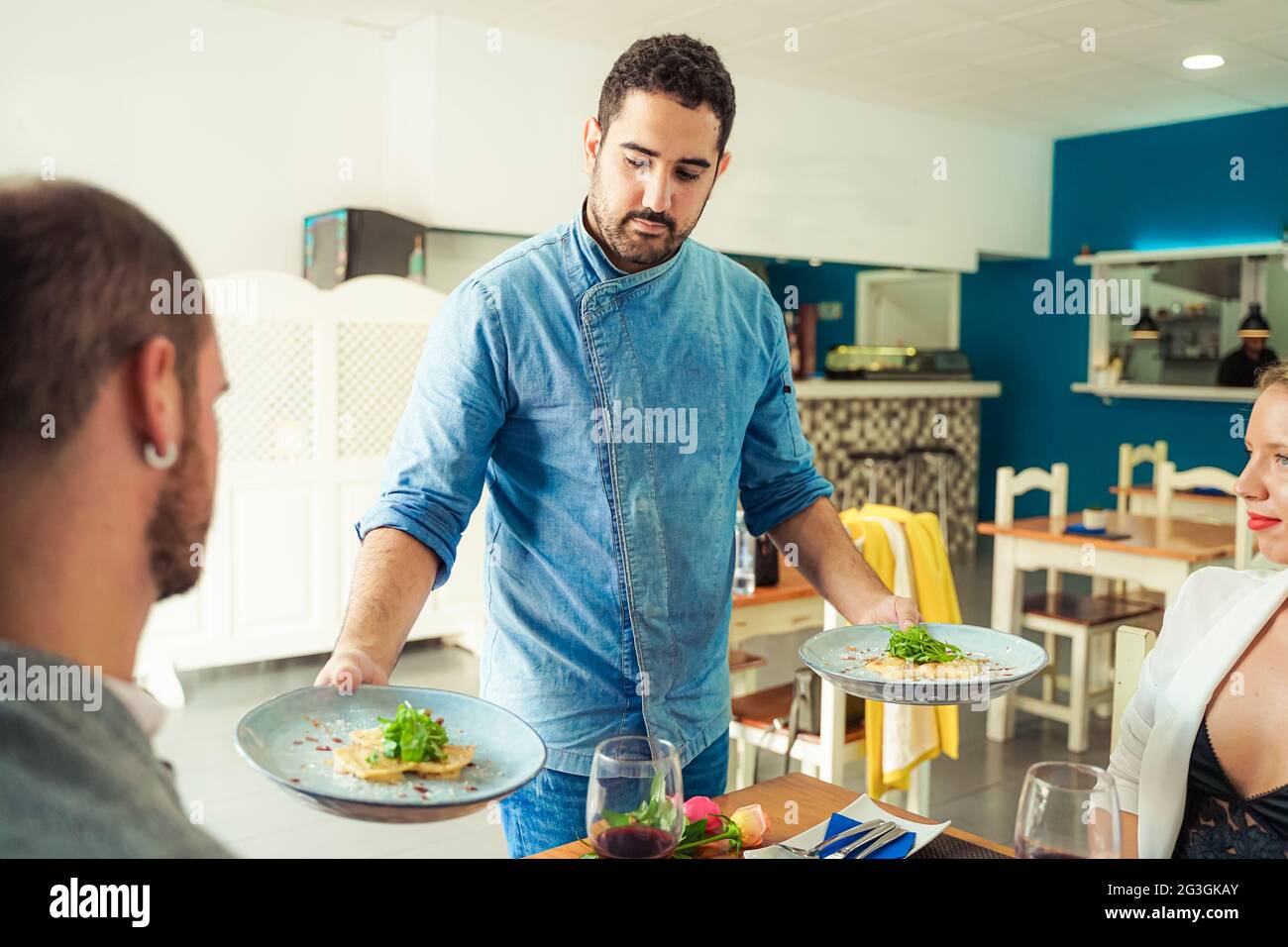 Waiter carrying two plates with pasta raviolis dish for younger couple