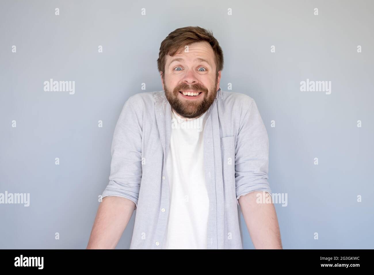 Funny, smiling man innocently shrugs shoulders and looks at the camera.  Gray background Stock Photo - Alamy