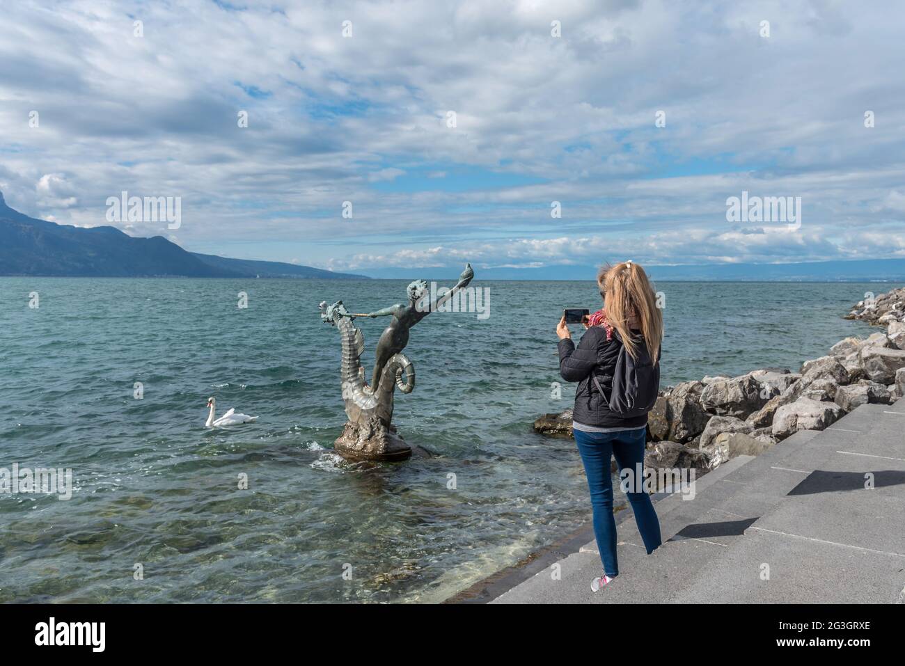 Vevey, Switzerland - October 11, 2020: Blonde woman taking a photo to Sculpture By Edouard-Marcel Sandoz At Vevey, Lake Geneva, Switzerland Stock Photo