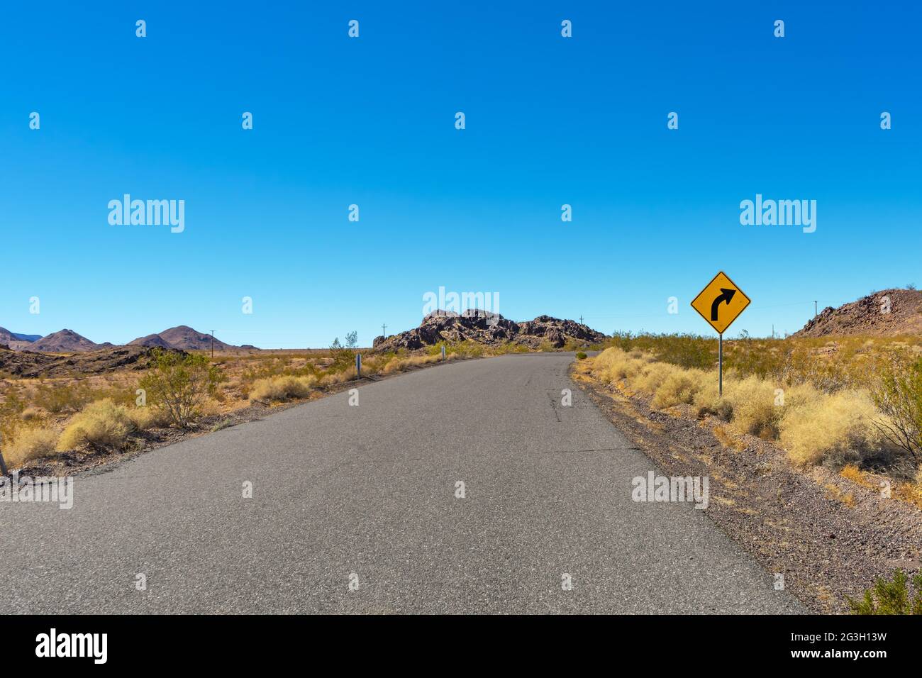 Road in the Mojave Desert with a caution sign and clear blue sky Stock Photo