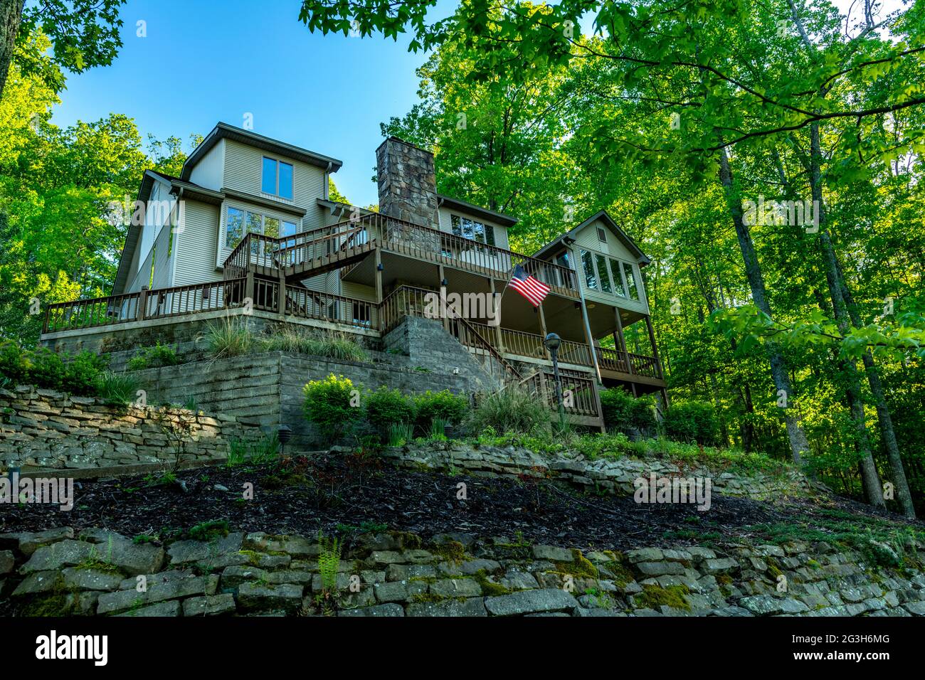 A home in the mountains of Tennessee sits perched atop a hillside in a forest of green oak trees and overlooking a panoramic lake. Stock Photo