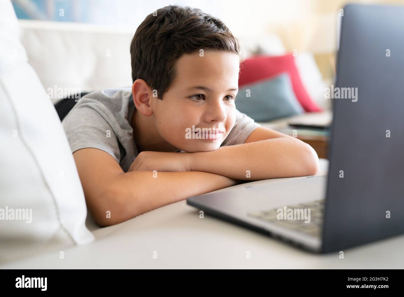 Picture of cute boy using laptop computer while lies on sofa at home ...