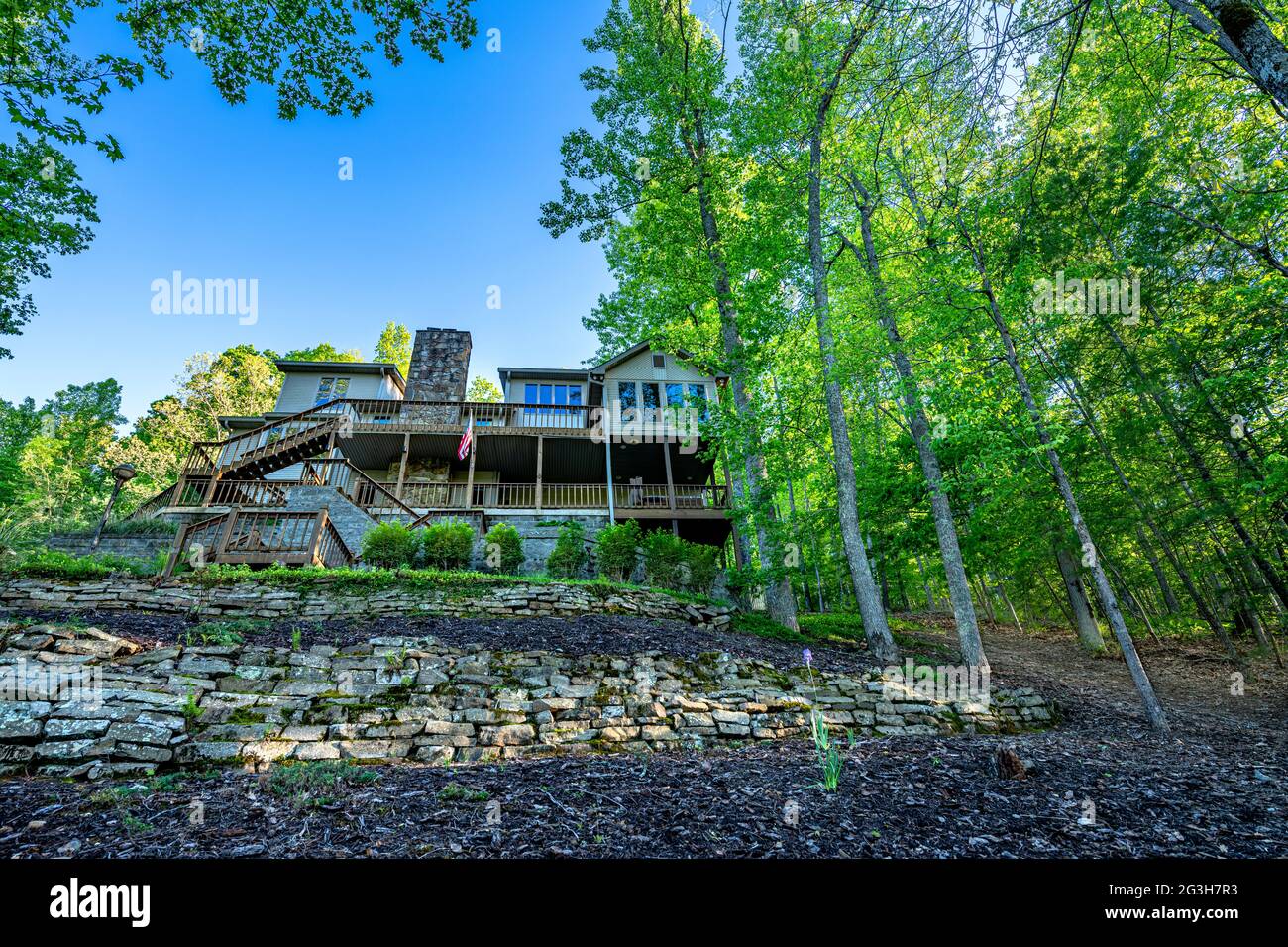 A home in the mountains of Tennessee sits perched atop a hillside in a forest of green oak trees and overlooking a panoramic lake. Stock Photo