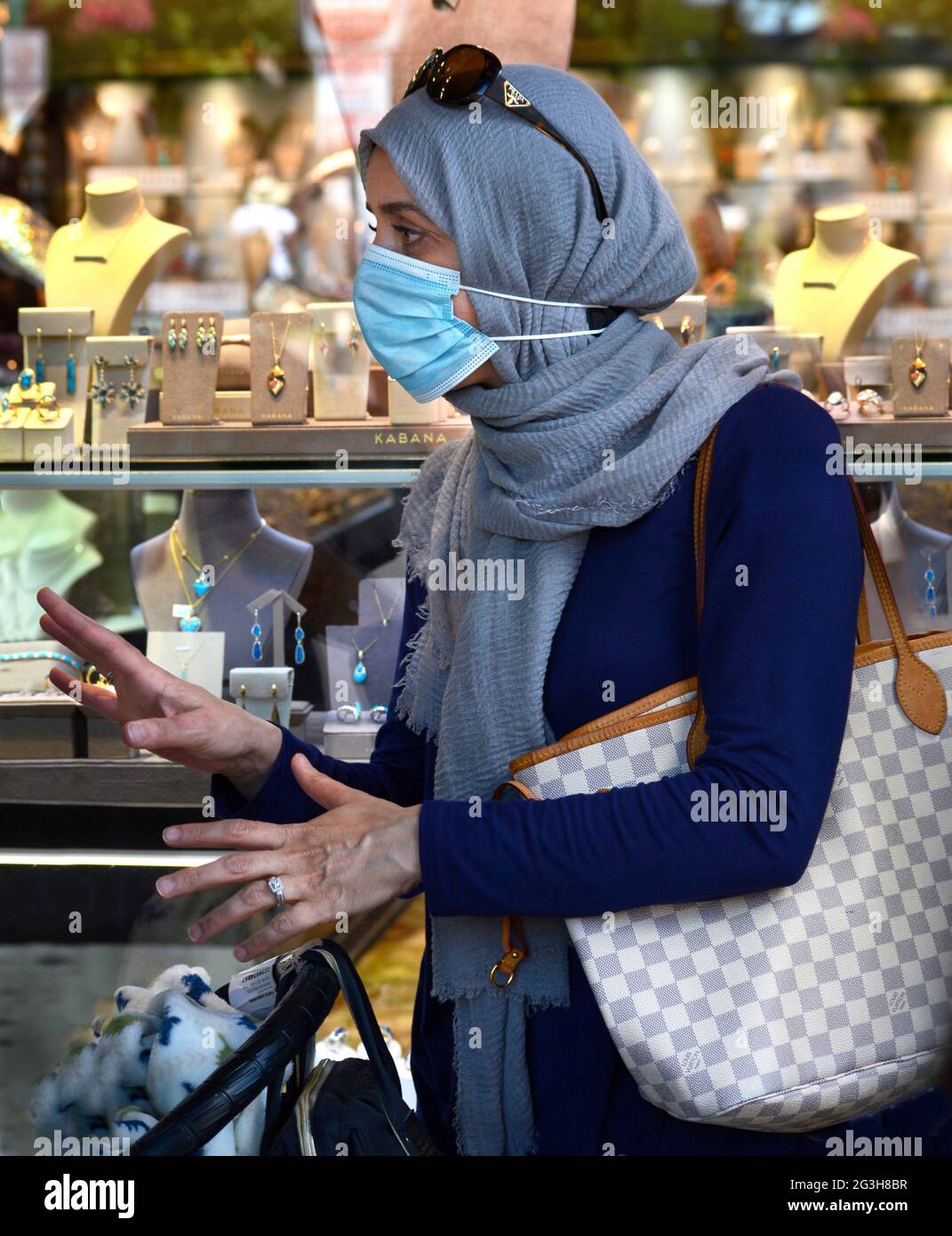 A muslim woman visiting Santa Fe, New Mexico, from the Middle East, window shops while wearing a pandemic mask and head wrap, or hijab Stock Photo