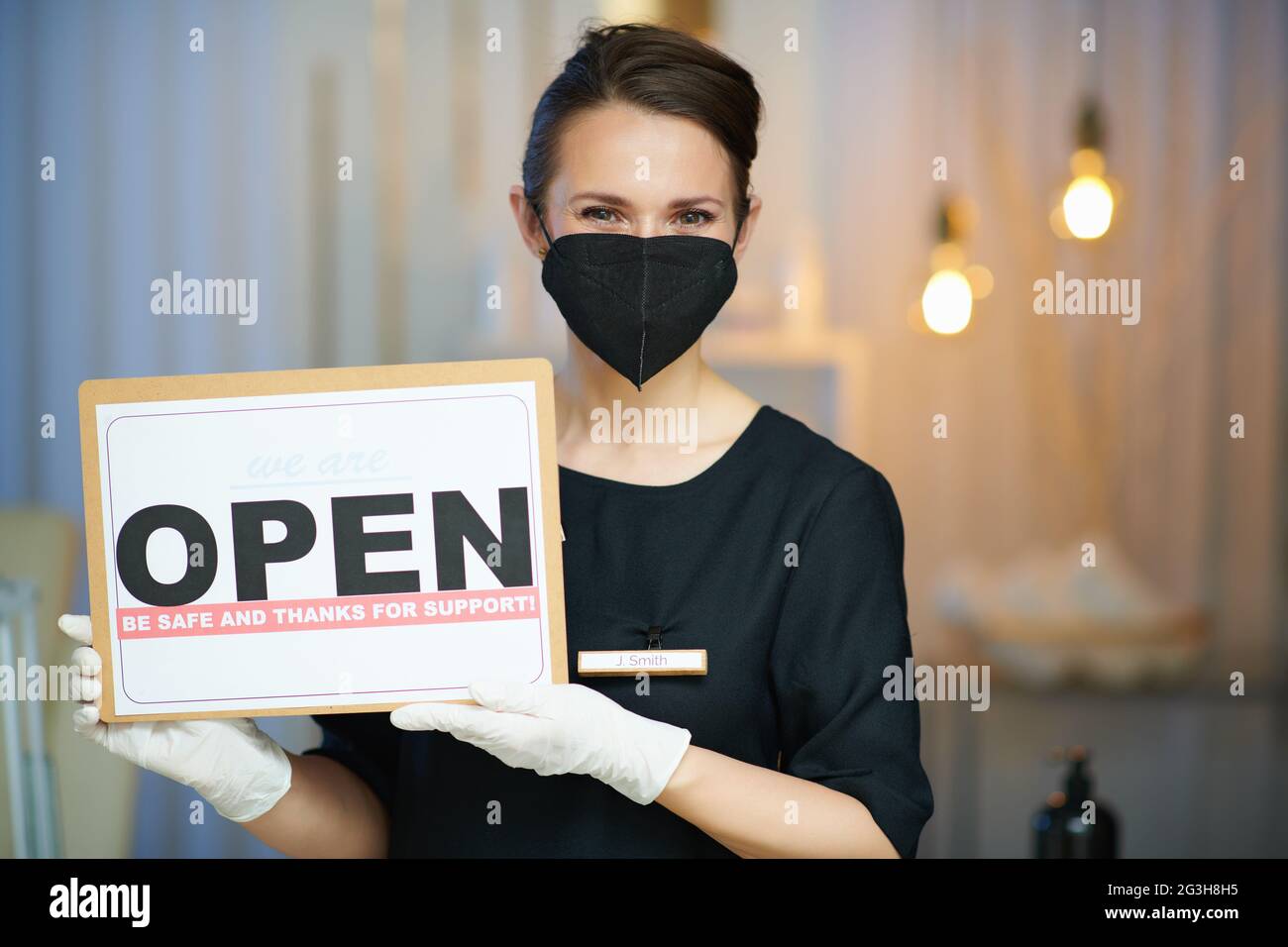 Business during covid-19 pandemic. Portrait of middle aged woman employee with ffp2 mask and open sign in modern beauty studio. Stock Photo