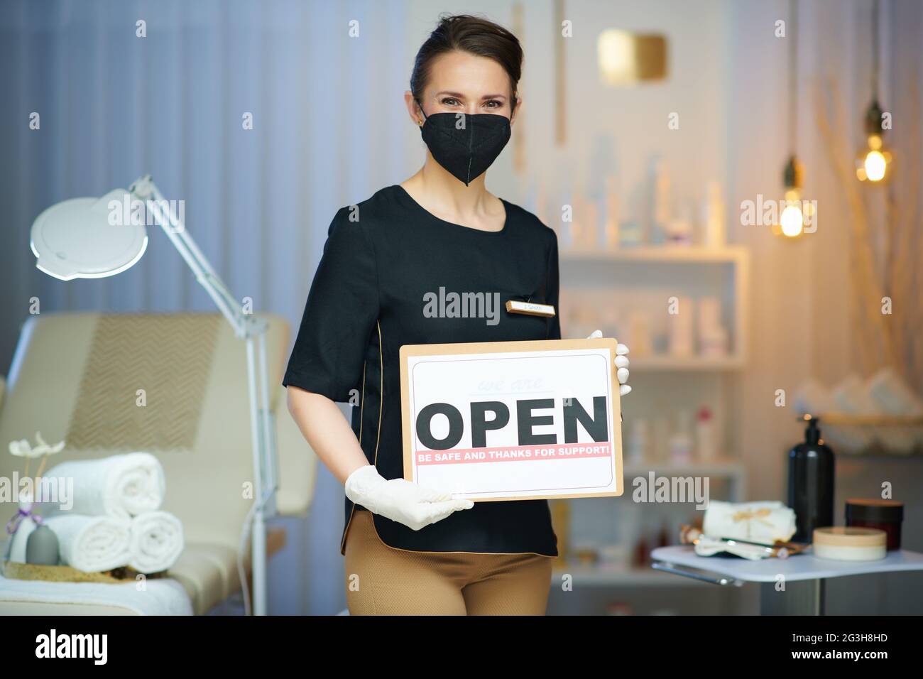 Business during coronavirus pandemic. woman worker with ffp2 mask and open sign in modern beauty salon. Stock Photo