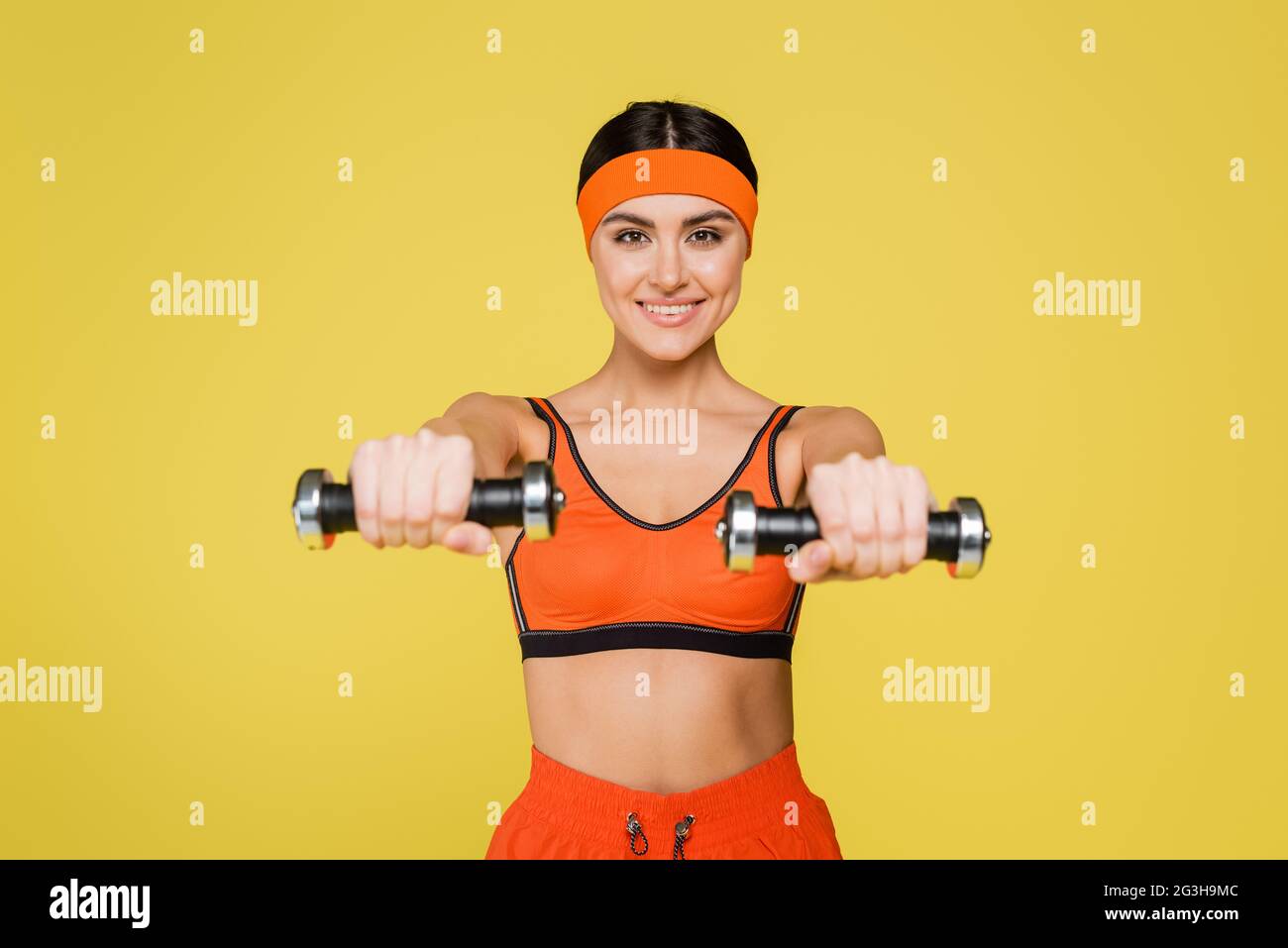 happy sportswoman looking at camera while working out with dumbbells