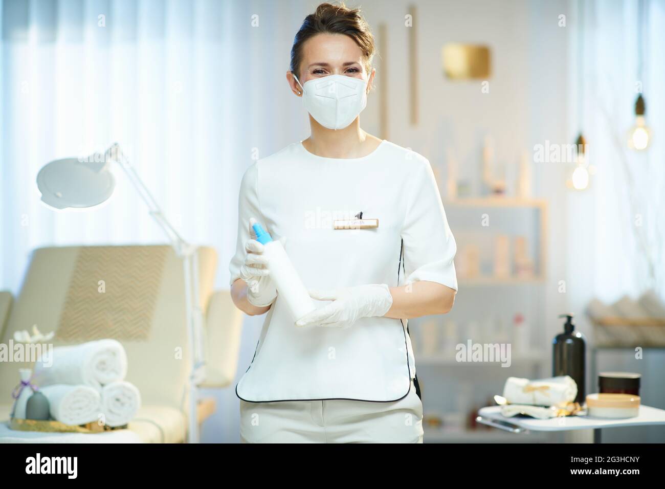 Business during coronavirus pandemic. female worker with ffp2 mask and sanitizer in modern beauty salon. Stock Photo