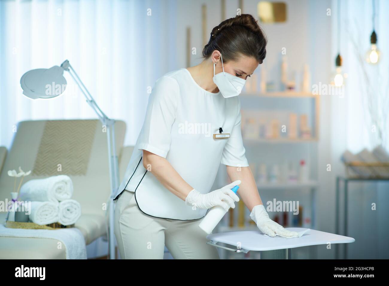 Business during coronavirus pandemic. female worker with ffp2 mask and disinfectant in modern beauty salon. Stock Photo