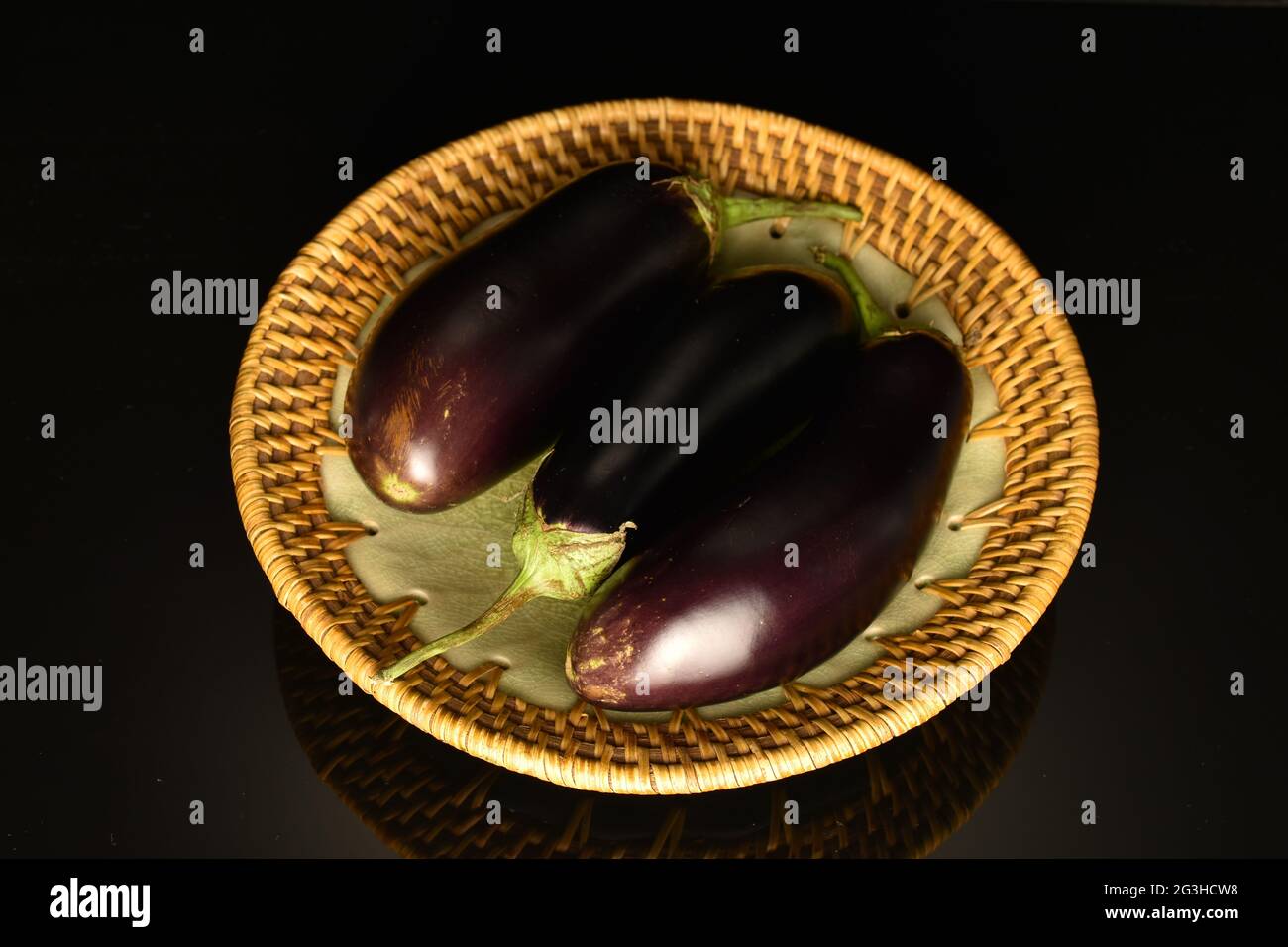 Three ripe dark blue eggplant on a ceramic plate, close-up, isolated on black. Stock Photo