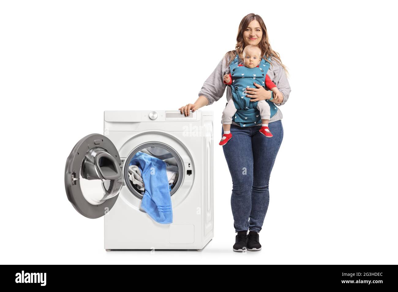 Full length portrait of a mother with a baby in a carrier standing next to a washing machine isolated on white background Stock Photo