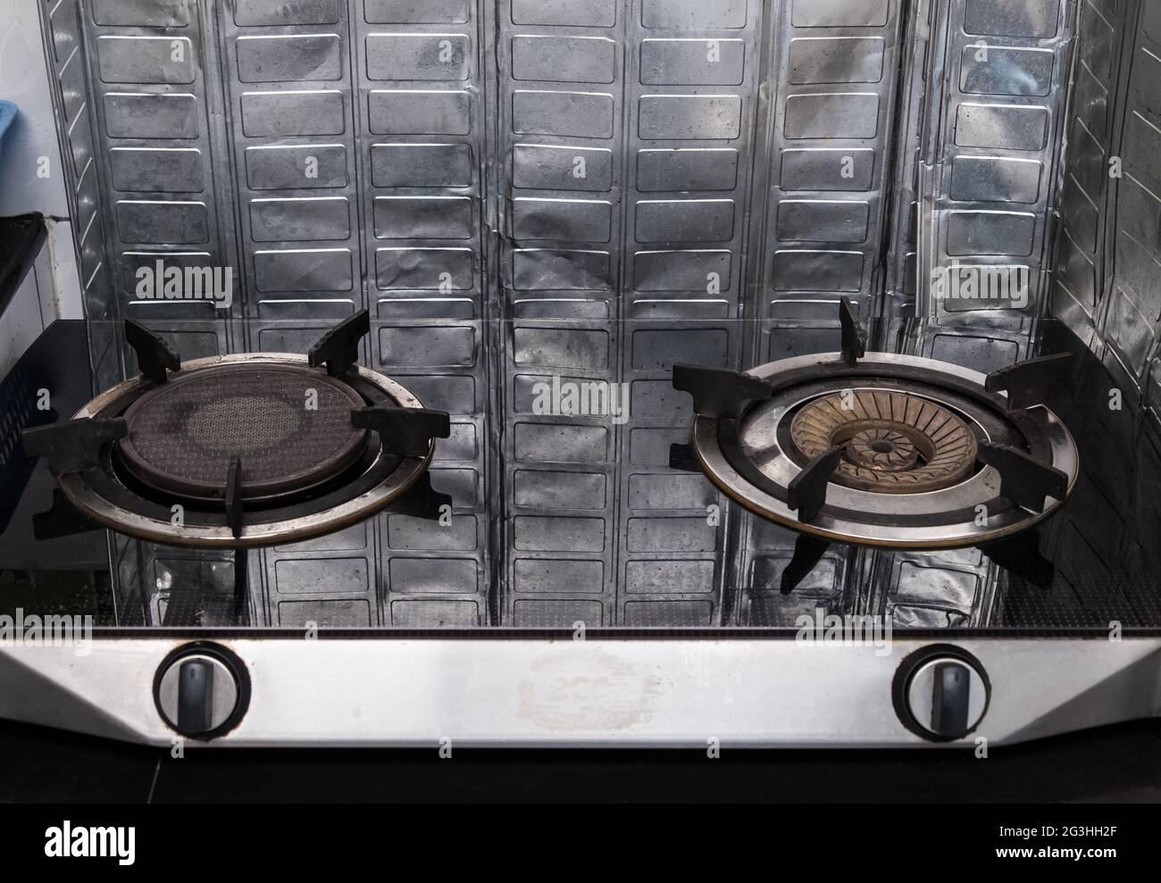 The old gas stove on the black counter with the foil partition is around to protect the cooking oil, reflection from the partition on the gas stove su Stock Photo