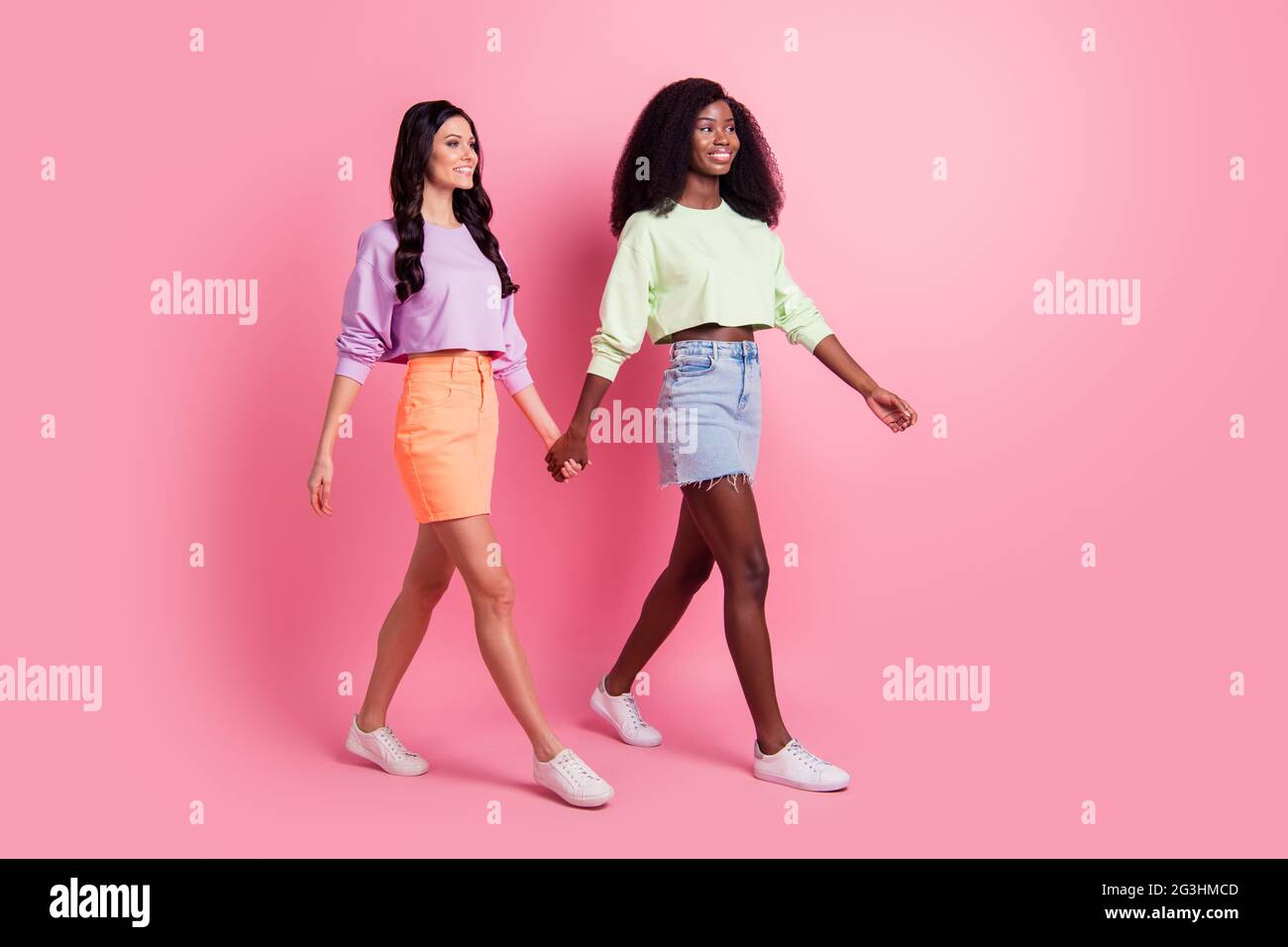 Full body profile side photo of cute charming nice ladies go empty space hold hands wear cropped jumper isolated on pink color background Stock Photo