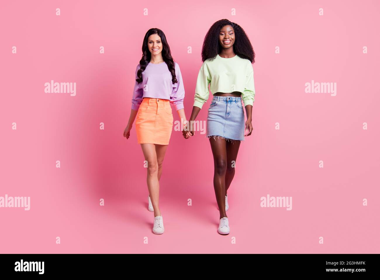 Full length photo of charming sweet girls go wear mini skirt hold hands  isolated on pink color background Stock Photo - Alamy