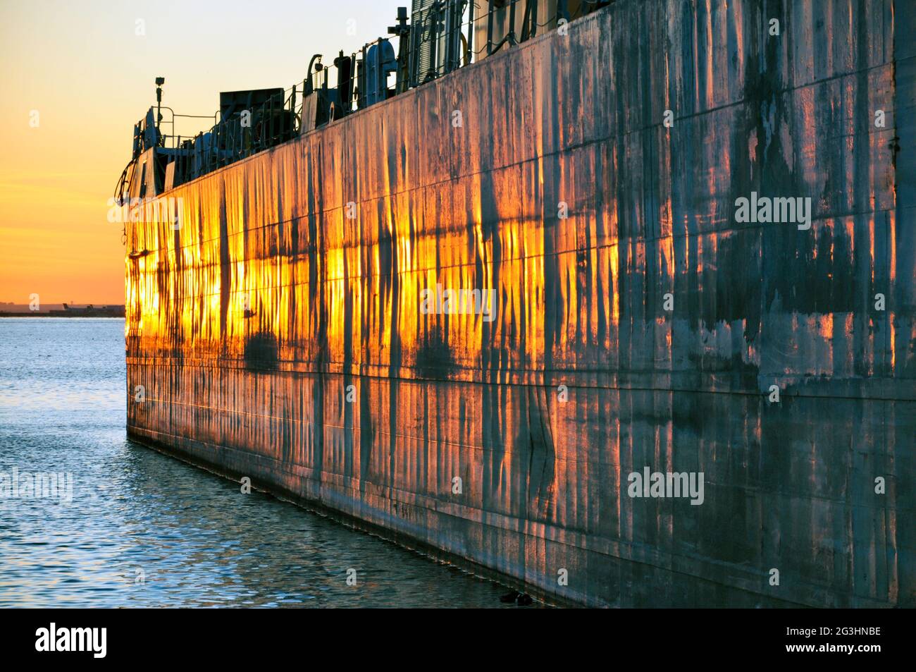 A bulk carrier laker ship is seen in the port of Toronto, glowing a fiery orange at sunset. Concept of maritime shipping. Stock Photo