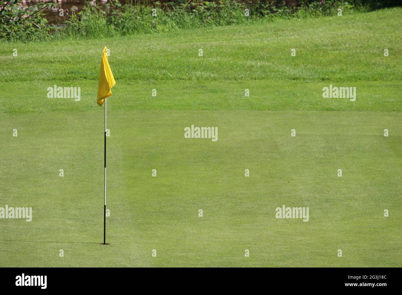 A photograph of a yellow flag on a neat golf course green Stock Photo