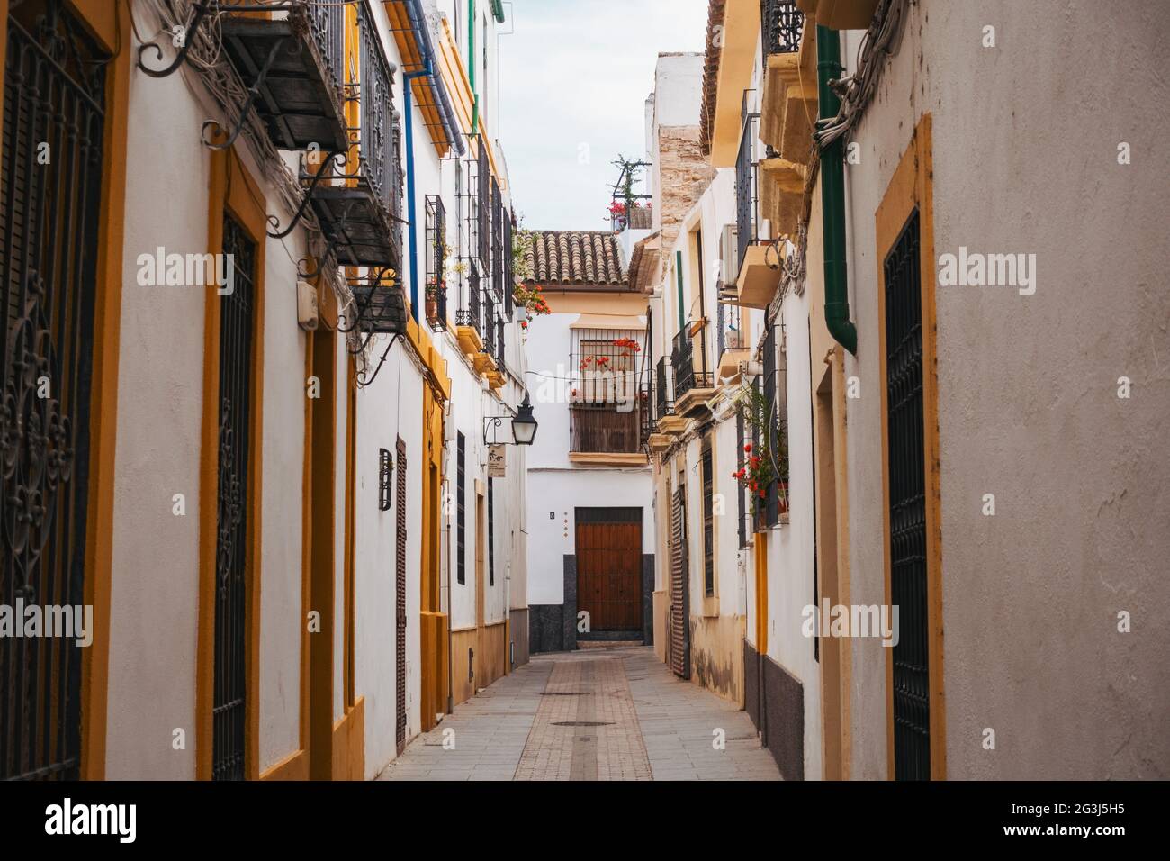 Building exteriors painted white and yellow line an empty narrow street in Córdoba, Spain Stock Photo