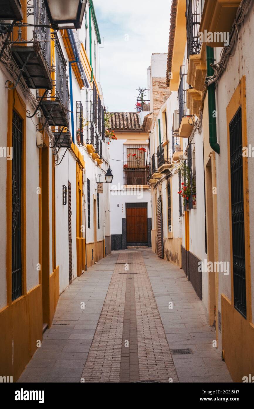 Building exteriors painted white and yellow line an empty narrow street in Córdoba, Spain Stock Photo