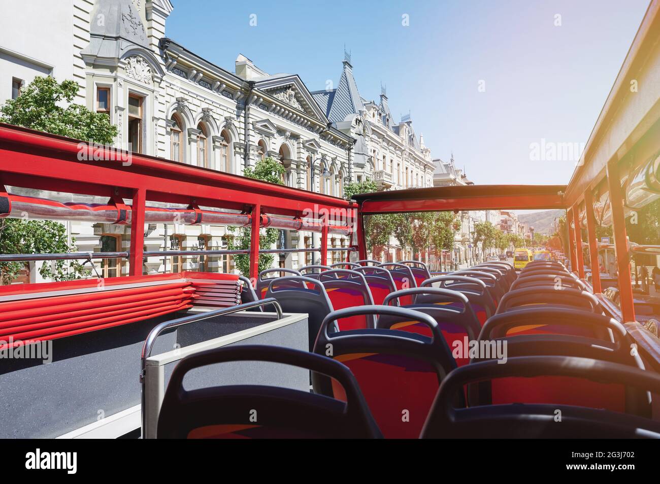 Empty red bus seats with open roof on old city background. Bus tour theme Stock Photo