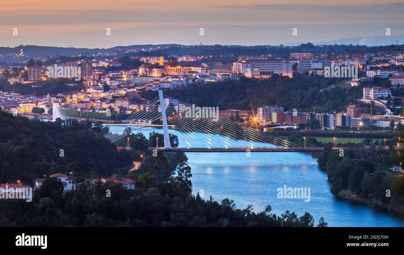 Panoramic view of Coimbra at dusk, in Portugal, with the Mondego river and the Rainha Santa Isabel bridge in the foreground. Stock Photo